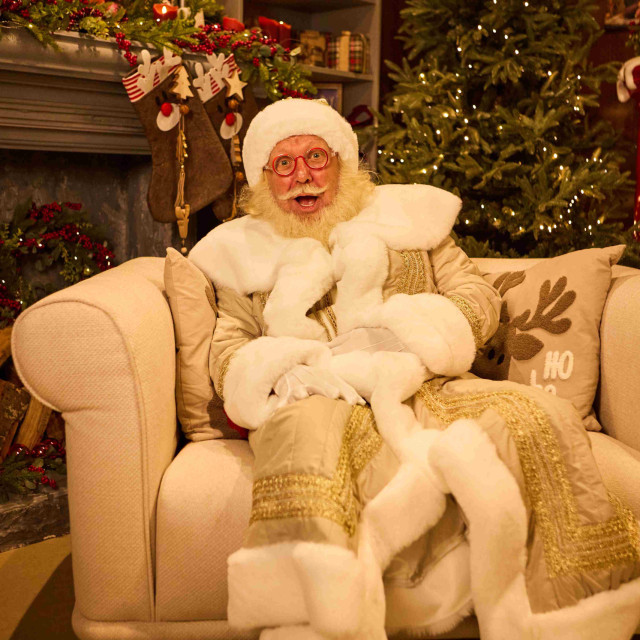 A man dressed in a Santa Claus suit is sitting in an armchair