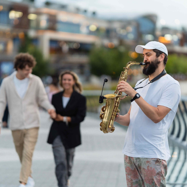 Passersby and a saxophonist on the Selfie Bridge in front of Kula Belgrade.